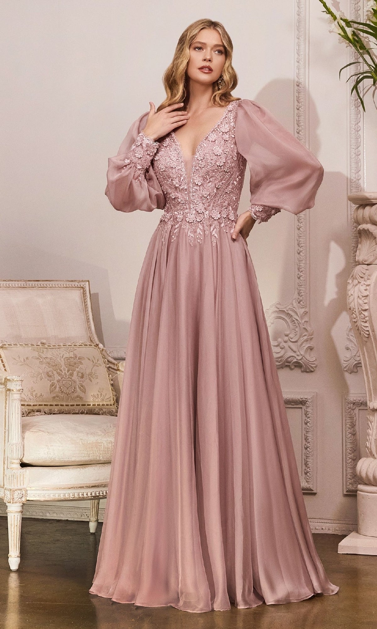 A woman in the Ladivine CD0183 modest long sleeve formal gown in mauve, featuring sheer puff sleeves and a lace bodice, stands elegantly—an ideal sophisticated mother of the bride choice.